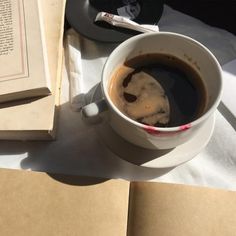 a cup of coffee sitting on top of a table next to an open book