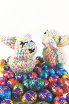 two crocheted animals sitting on top of some chocolate eggs with colorful candies around them