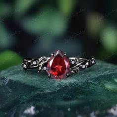 a close up of a ring with a red stone in it on a leafy surface