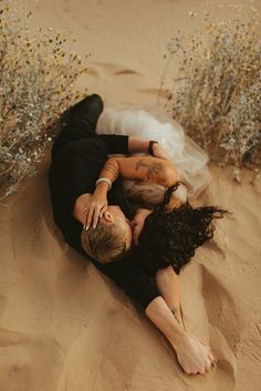 a man and woman laying in the sand with their hands on each other's shoulders