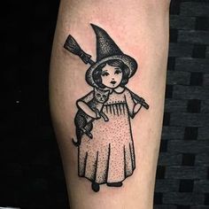 a black and white tattoo of a girl with a cat on her arm holding a broom