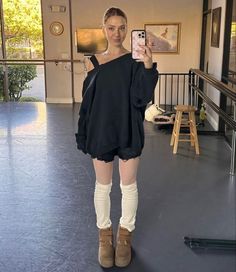 a woman taking a selfie with her cell phone in an art gallery while wearing short shorts and knee high socks