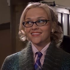 a woman wearing glasses and a purple tie smiles at the camera while standing in an elevator