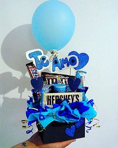 a person holding up a box filled with candy, candies and balloons in front of a white wall