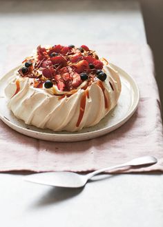 a cake with fruit on top sitting on a plate next to a fork and spoon