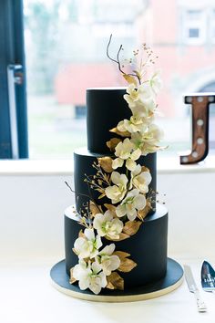 a three tiered black cake with white flowers on top