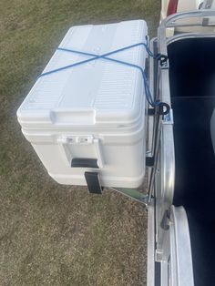 a white cooler sitting in the back of a boat on top of grass and dirt