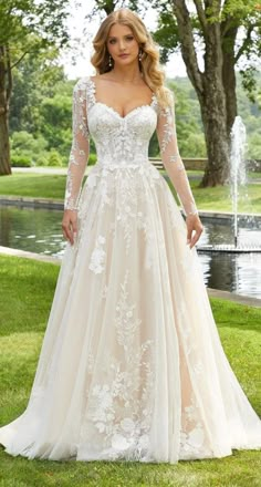 a woman in a wedding dress standing on the grass with trees and water behind her