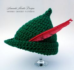 a crocheted green hat with a red feather