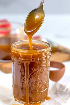 a spoon full of caramel sauce being poured into a jar