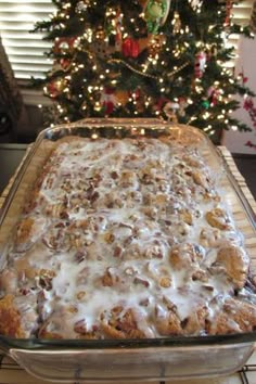 a christmas tree is in the background behind a glass pan filled with baked goods and icing