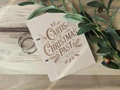 a wooden card with the words christmas past on it next to two wedding rings and an olive branch