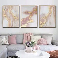 three paintings hang on the wall above a couch in a white living room with pink and gold accents