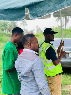 three men standing under an umbrella talking to each other