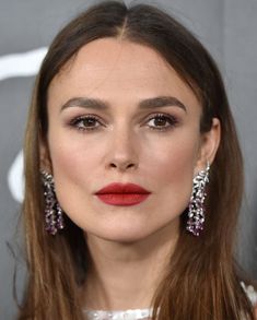 a woman with long brown hair and red lipstick wearing large earrings on her head, looking at the camera