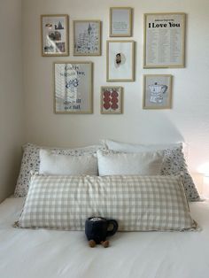 a white bed topped with lots of pillows next to pictures on the wall above it