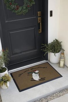 a door mat with a snowman on it and two potted plants next to it