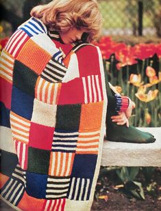 a woman sitting on a bench wearing a colorful blanket