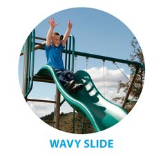 a young boy sitting on top of a green slide at a play ground with his arms in the air