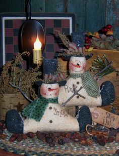 a couple of snowmen sitting on top of a table next to a lit candle