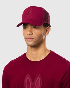 A person wearing a stylish burgundy Psycho Bunny cap adorned with a rabbit logo, paired with a matching shirt. The breathable mesh design of the MENS MALTON TRUCKER CAP - B6A797D200 adds flair to the ensemble, with both items featuring rabbit designs. The plain light gray background is perfect for showcasing this active lifestyle accessory. Bunny Man, Bunny Logo, Cap For Men, Bold Color, Active Lifestyle, Trucker Cap, Bold Colors, Style Guides, Mens Accessories