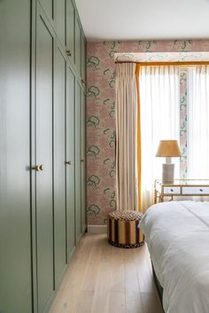 a bed room with a neatly made bed next to a large window and a lamp