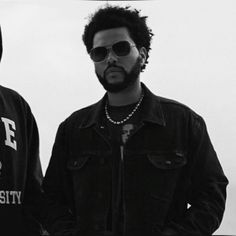 two men standing next to each other in front of a white wall and wearing sunglasses