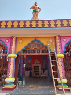 a woman standing on top of a colorful building next to a tall wooden ladder in front of it