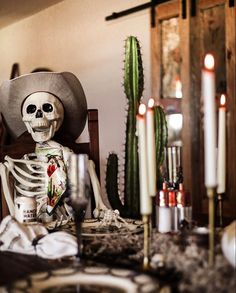 a skeleton sitting in a chair next to a cactus and some candles on a table