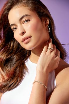 a woman with long brown hair wearing a white top and gold hoop earrings on her left hand