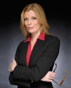 a woman in a black suit and red shirt with her arms crossed looking at the camera