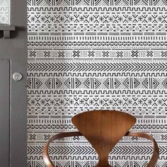 a wooden chair sitting in front of a wall with a black and white pattern on it