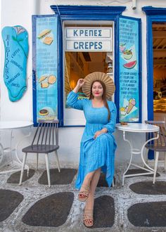 a woman in a blue dress and straw hat sitting on a bench outside a restaurant