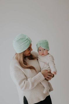 a woman holding a baby wearing a green knitted beanie and black leggings