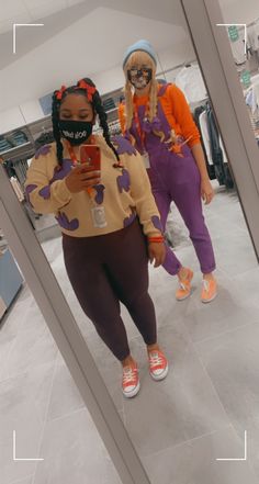 two women standing in front of a mirror looking at their cell phones while wearing matching outfits