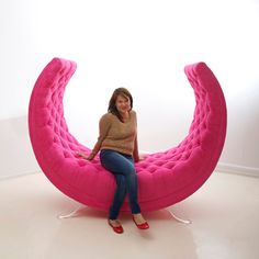 a woman sitting on a pink couch in the middle of a room with white walls