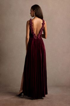 the back of a woman wearing a long dress with an open neck and deep red velvet skirt