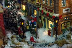 a toy town with people riding bicycles and cars in the snow at night time,