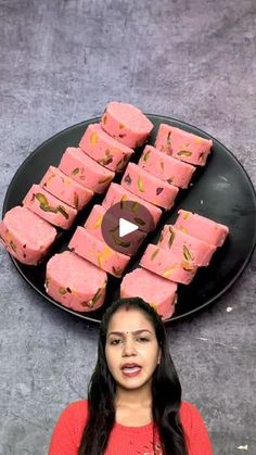 a woman standing in front of a black plate filled with pink and gold desserts