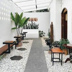 a long walkway between two buildings with tables and benches on each side, surrounded by potted plants