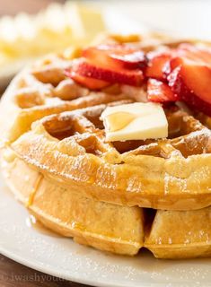 a stack of waffles topped with butter and sliced strawberries on a white plate