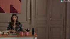 a woman sitting at a desk in front of a wall with pink and red designs