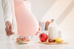 the pregnant woman is preparing to eat her fruit and milk while holding her belly up