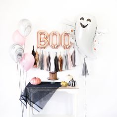 balloons and streamers are on the wall above a table with a boo balloon, tassels, and other decorations