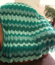 someone is holding up a green and white crocheted blanket