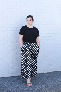 a woman standing in front of a white brick wall wearing black and white polka dot pants