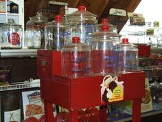 several large glass jars are stacked on top of a red cart in a store filled with other items