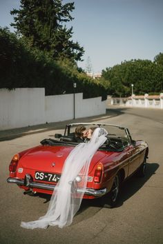 a bride and groom kissing in the back of a convertible car