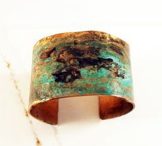 Our wide bronze cuff is hand forged and given a unique textured finish. The piece is then given a rich verdigris patina which ranges in color from black, to deep browns and vibrant greens. The aging process creates a different, organic patina on each piece. No two bracelets are exactly alike. A true one of a kind just like you. This is a great idea for a bronze anniversary gift. Each piece is sealed to protect it's finish. However, to preserve the patina it is best not to wear the piece while sw Artistic Patina Cuff Bracelet As Gift, Artistic Patina Cuff Bracelet Gift, Vintage Bronze Cuff Bracelet With Patina, Bronze Patina Cuff Bangle Bracelet, Gold Copper Cuff Bracelet With Patina, Green Patina Cuff Bracelet As Gift, Green Patina Cuff Bracelet Gift, Brass Cuff Bracelet With Patina As A Gift, 19th Anniversary Gifts