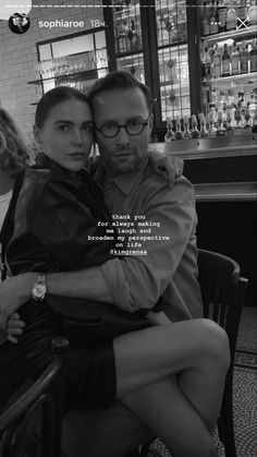 a man and woman sitting next to each other on a chair in front of a bar